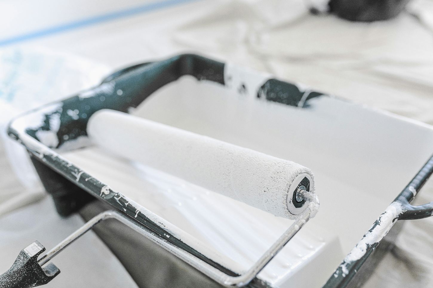 Close-up of a paint roller and tray with white paint
