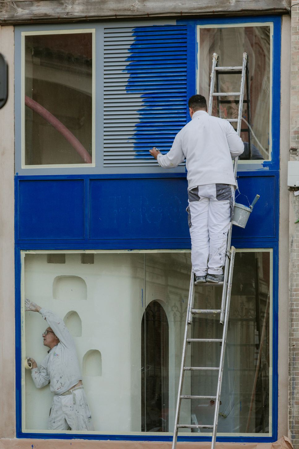 Exterior storefront being painted blue from a ladder